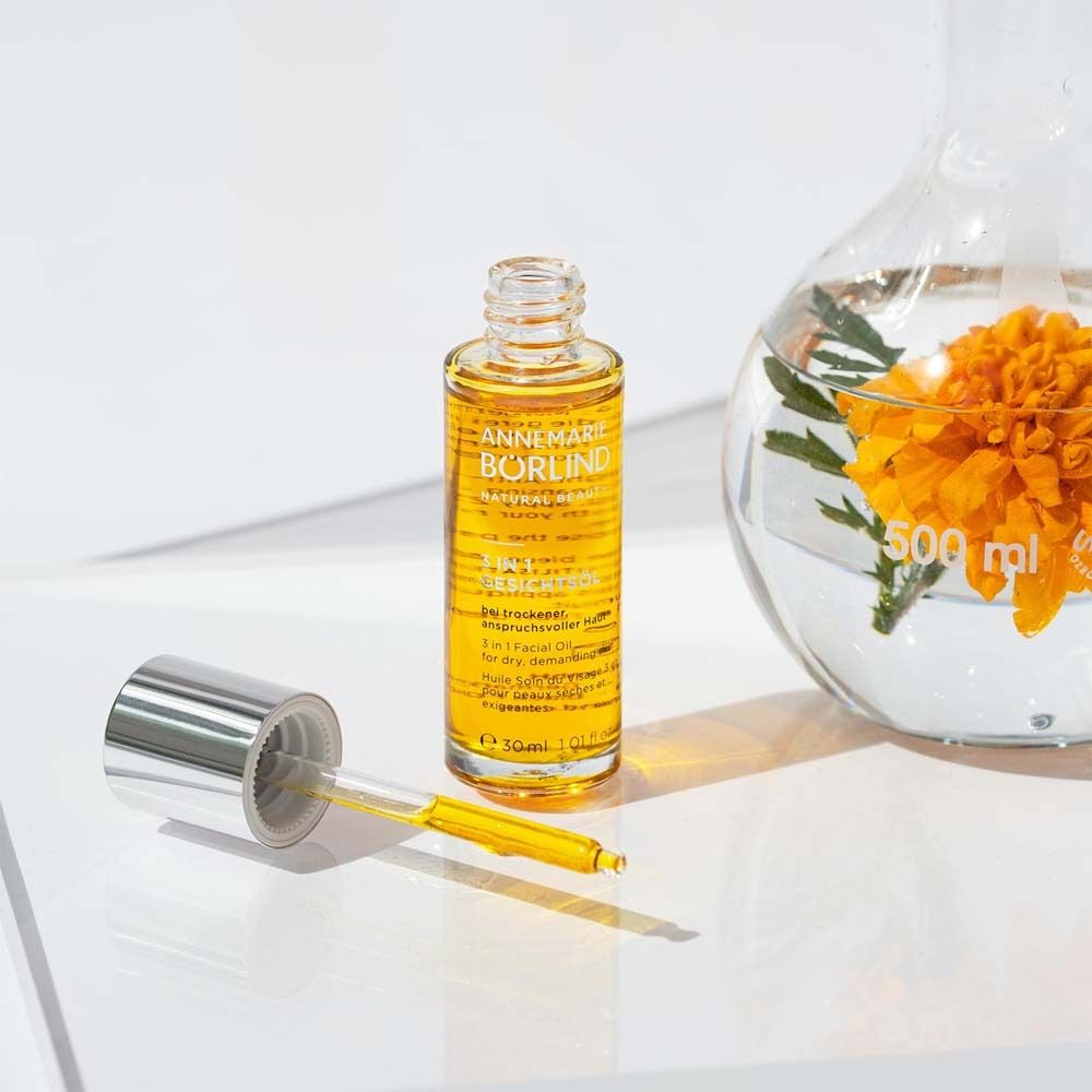 Flacon d'huile pour le visage avec pipette à côté d'un bécher avec une fleur. Produit : ANNEMARIE BÖRLIND, 3 en 1 Huile Visage.