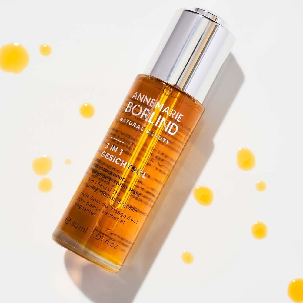 Flacon d'huile pour le visage avec gouttes jaunes. Produit : ANNEMARIE BÖRLIND, 3 en 1 Huile Visage. Flacon avec bouchon argenté.