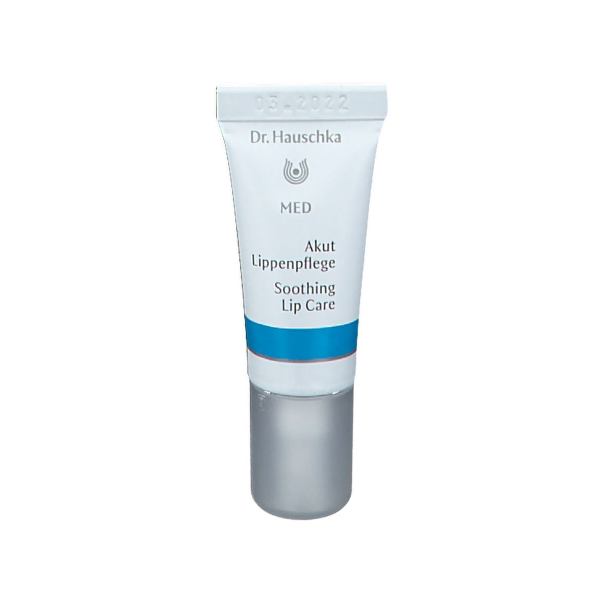 Tube blanche avec bande bleue. Inscriptions: Dr. Hauschka, MED, Akut Lippenpflege, Soothing Lip Care. Bouchon gris.