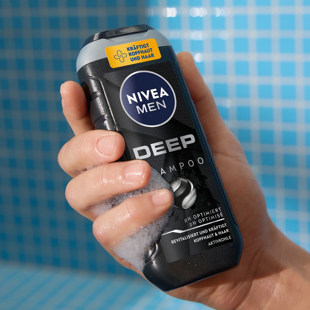 Main tenant un flacon NIVEA MEN DEEP Shampoo avec mousse. pH optimisé au charbon actif.