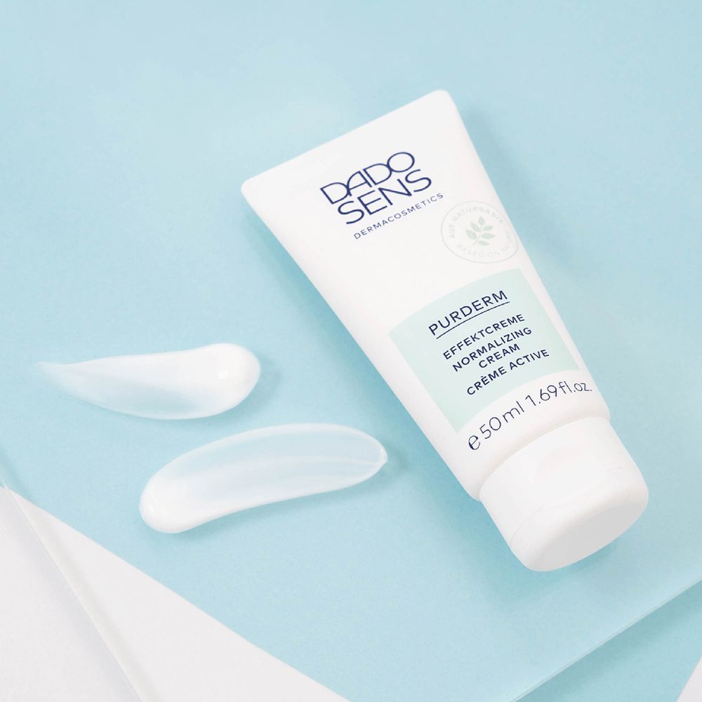 Taches de crème blanche à côté du tube. Tube avec logo DADO SENS et nom du produit. Fond bleu clair.