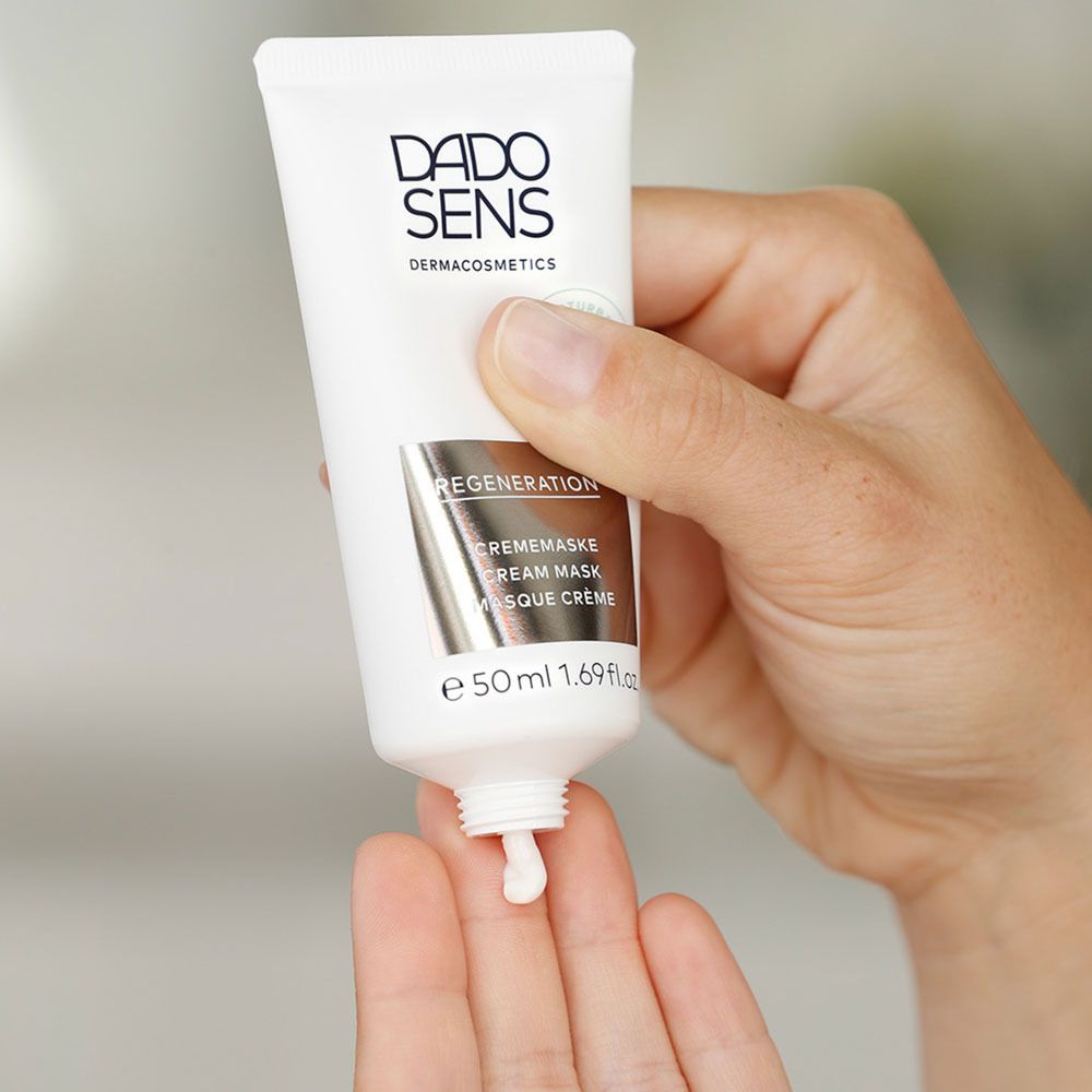 Main tenant un tube DADO SENS REGENERATION. Crème sortant du tube.