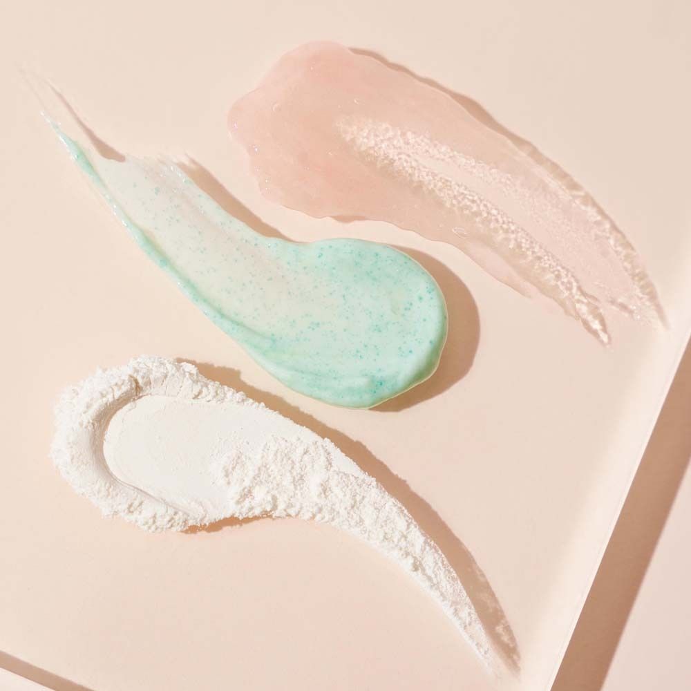 Trois éclaboussures de couleur : gel rose, gommage vert, poudre blanche. Fond : rose clair.