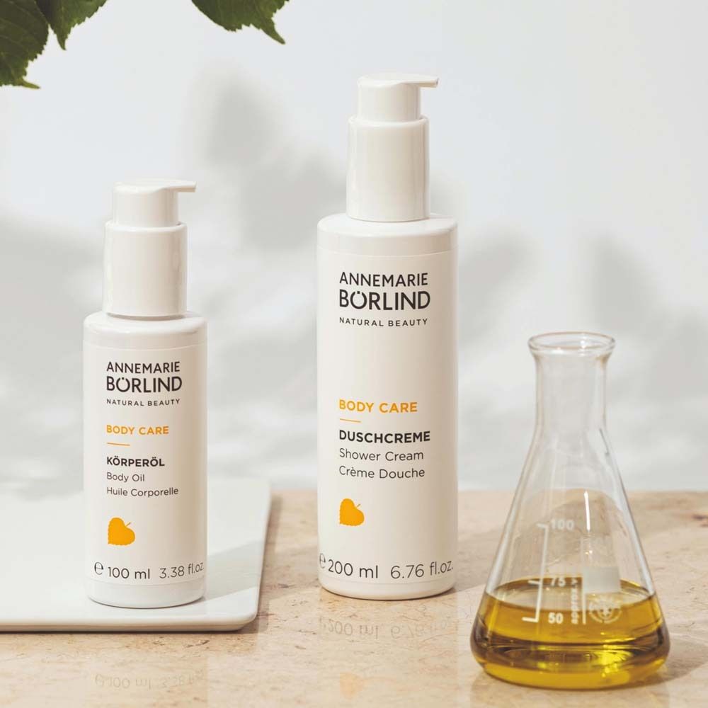 Deux flacons blancs et un récipient en verre. Inscription : ANNEMARIE BÖRLIND, BODY CARE. Logo jaune.