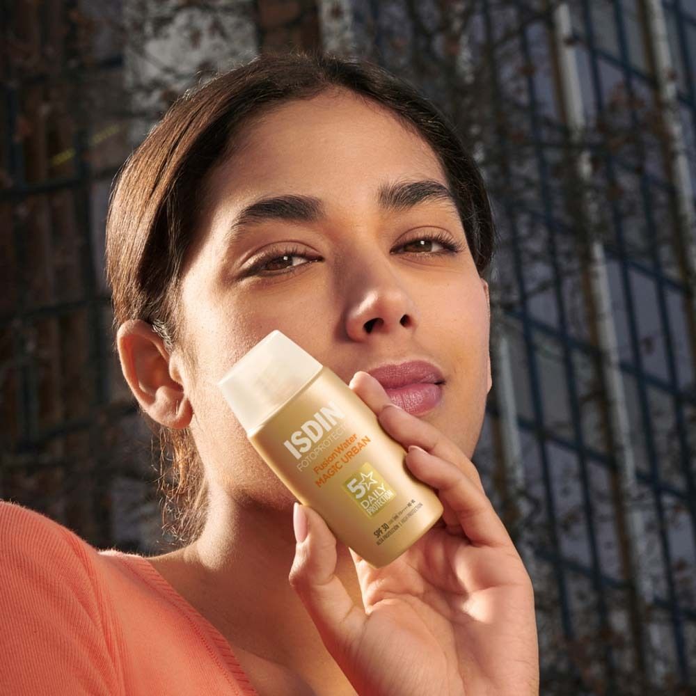 Femme tenant un flacon de crème solaire doré. Le flacon porte la mention ISDIN Fotoprotector Fusion Water Magic Urban.