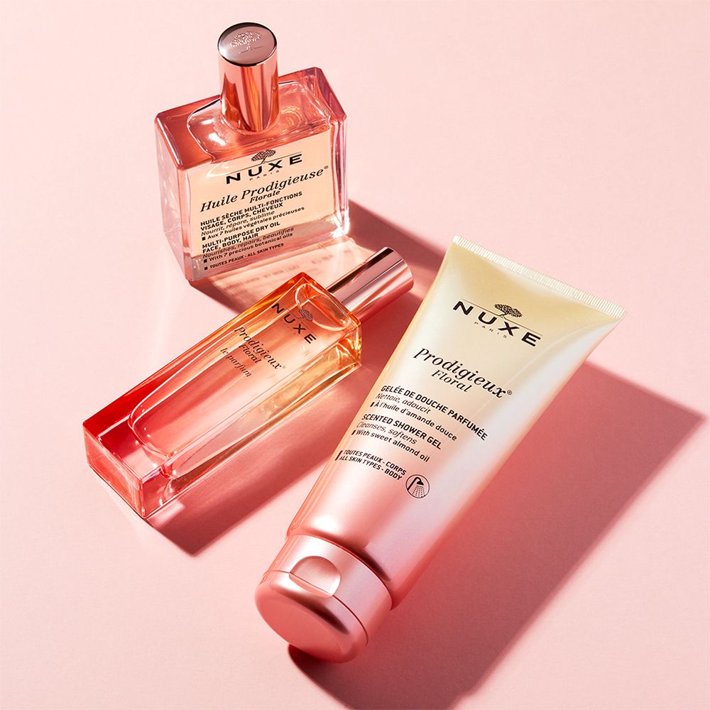 Trois produits NUXE : gel douche, huile et parfum. Emballages roses et dorés. Marque visible.