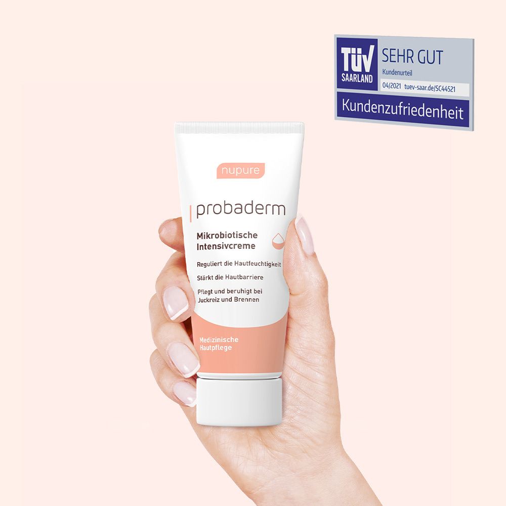 Main tenant un tube de crème. Inscription : nupure probaderm, Crème intensive microbiotique. Sceau TÜV.