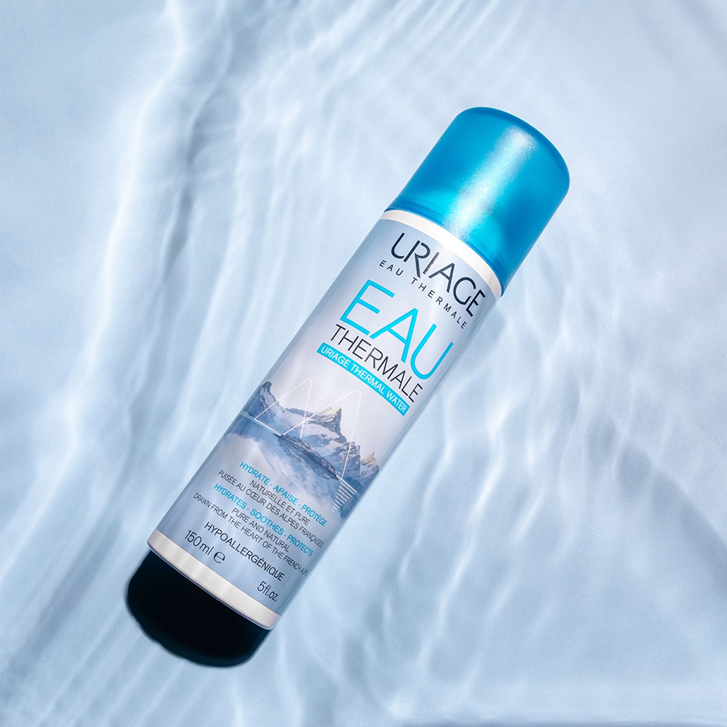 Spray Uriage Eau Thermale dans l'eau. Flacon bleu et blanc. Texte: Eau Thermale, 100% pur et naturel.