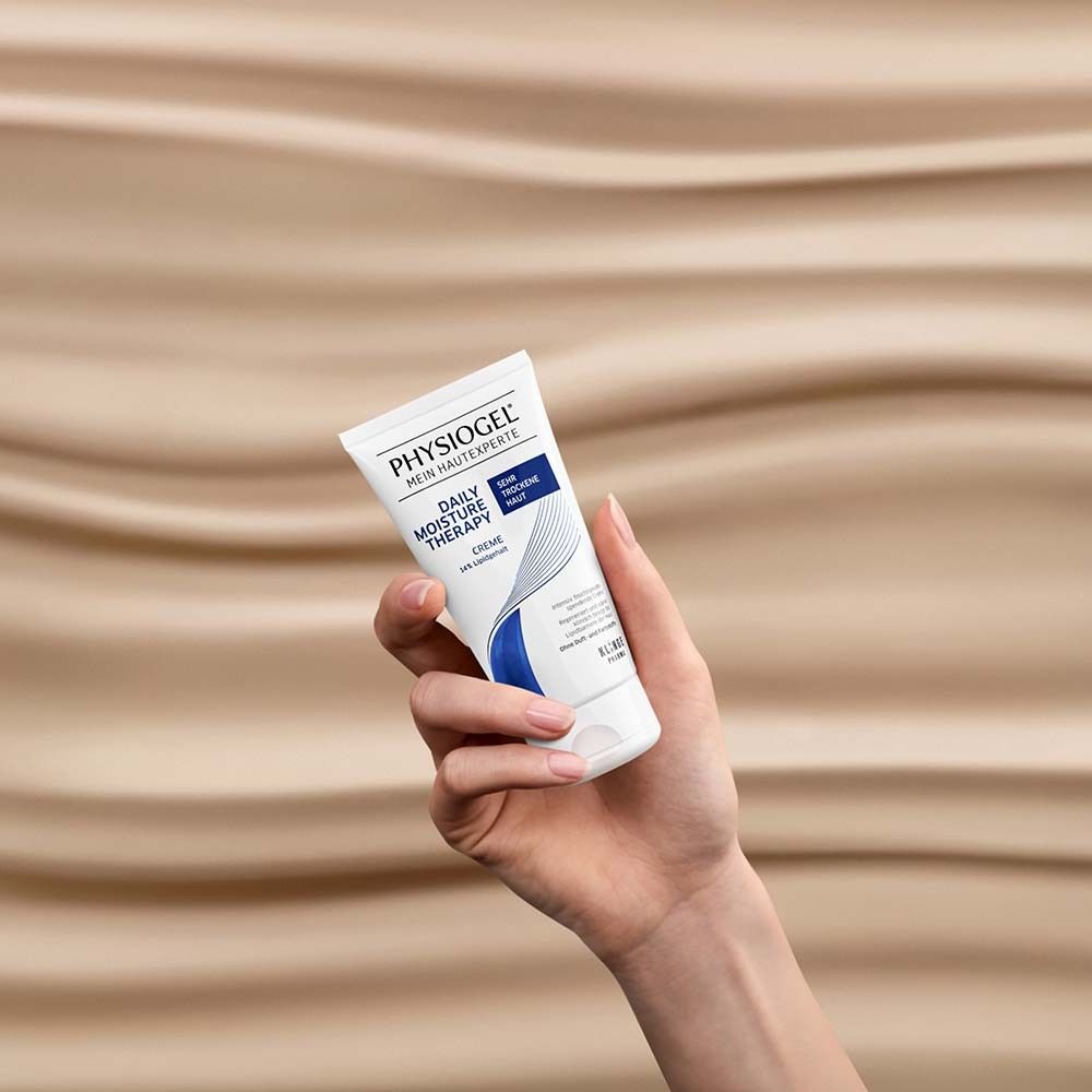 Main tenant un tube de crème PHYSIOGEL®. Fond : ondulé, beige.