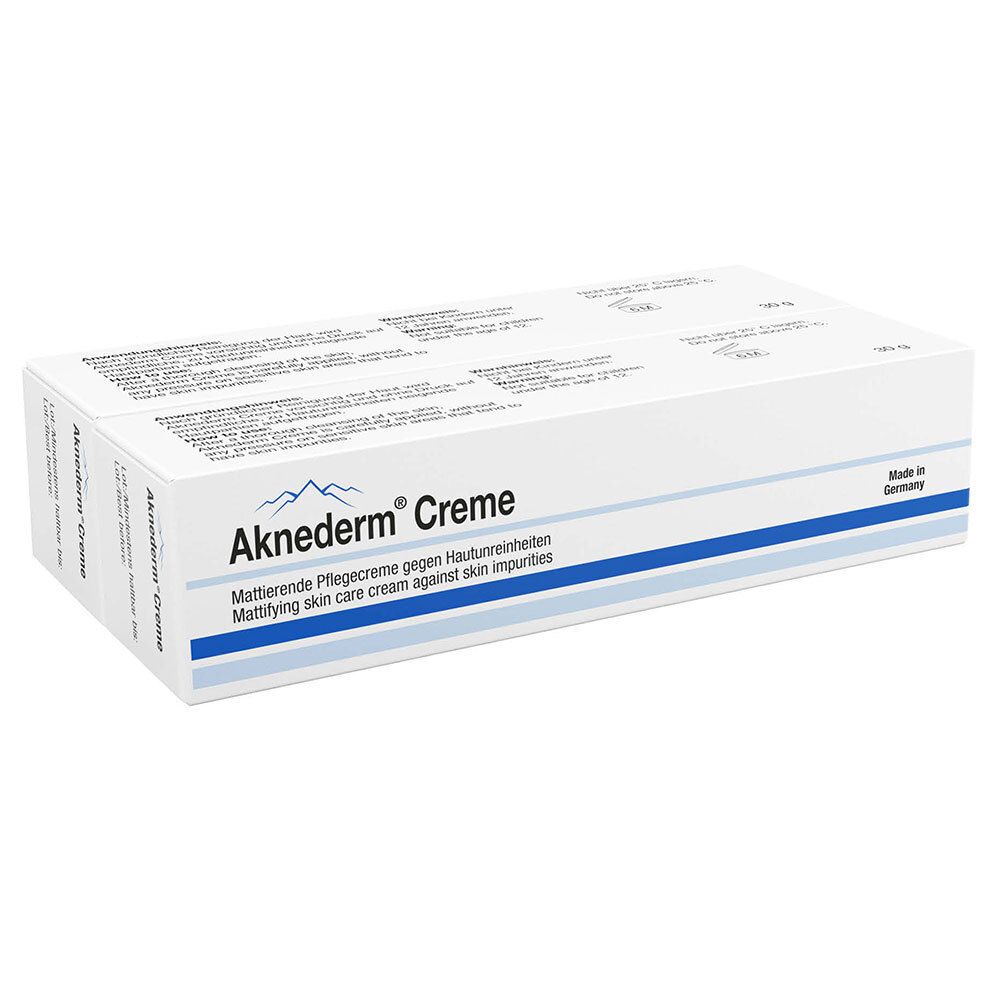 Boîte pliante blanche avec nom et description du produit. Bandes bleues. Inscription : Aknederm® Creme.