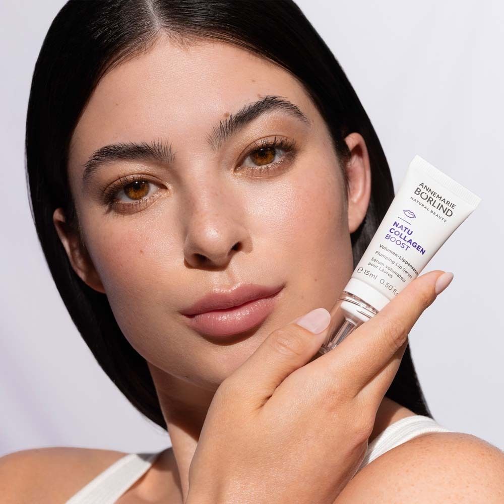 Femme tenant un sérum pour les lèvres. Marque : ANNEMARIE BÖRLIND. Nom du produit : NATU COLLAGEN BOOST. Femme au teint clair.