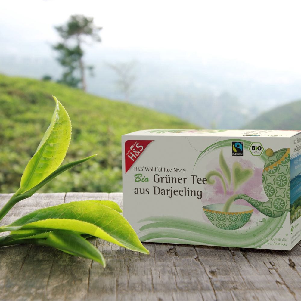 Emballage H&S Bio Thé Vert de Darjeeling sur table en bois avec feuilles de thé.