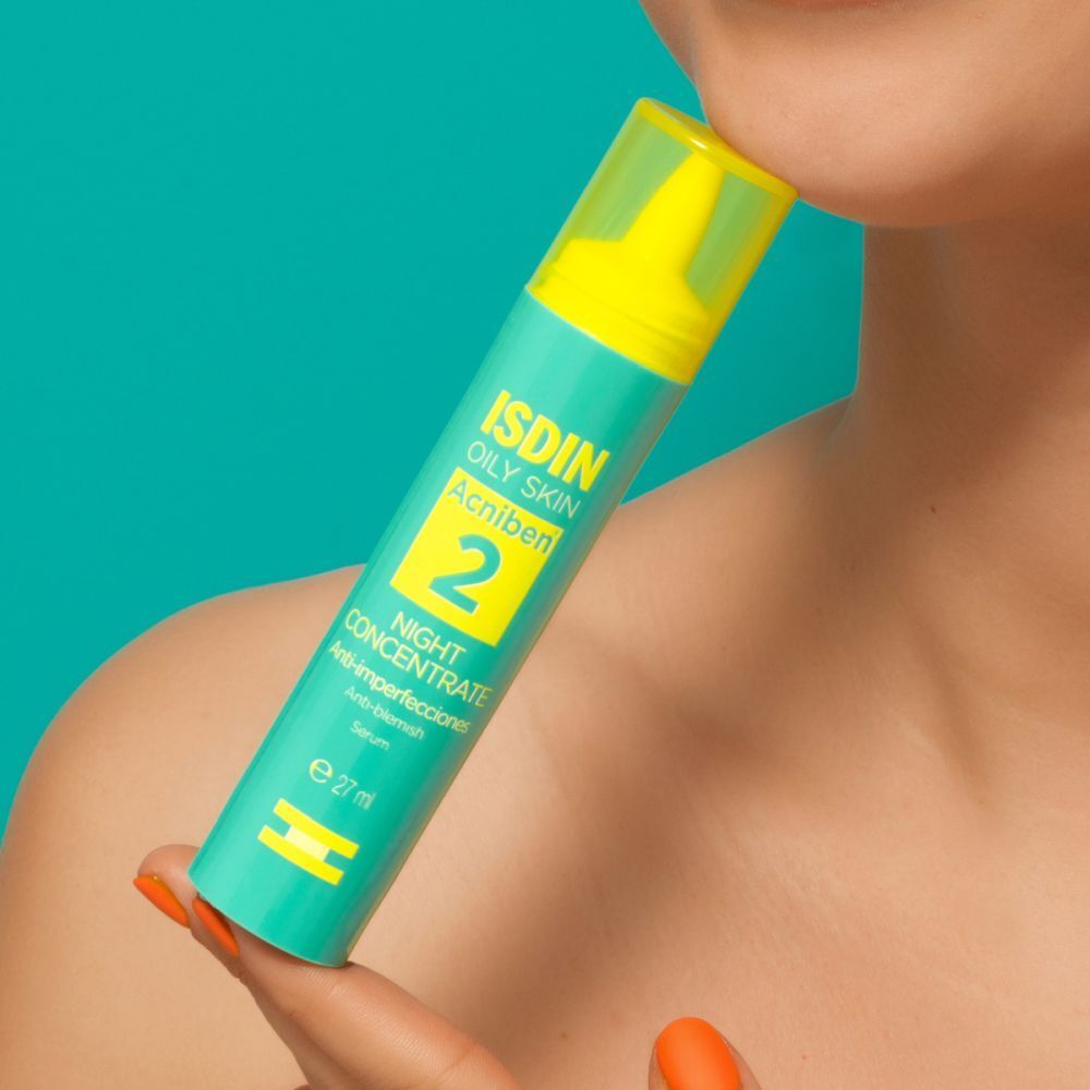 Flacon turquoise avec bouchon jaune. Inscription : ISDIN, ACNIBEN 2, Night Concentrate. Tenue par une personne.