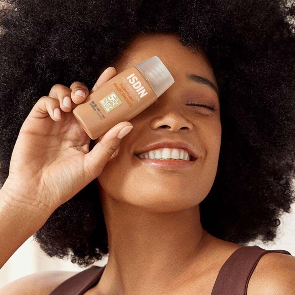 Femme avec ISDIN Fusion Water Magic Bronze. Elle tient le flacon devant son œil.
