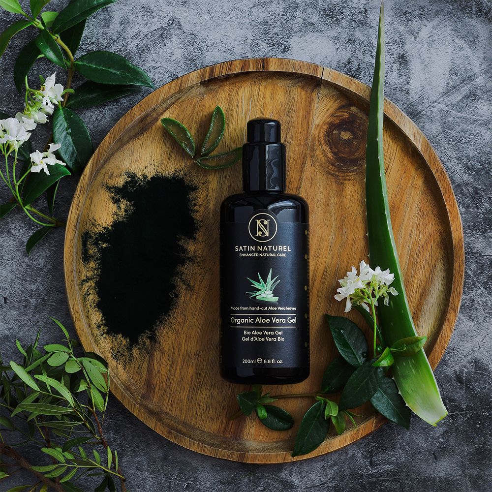 Flacon Gel Bio Aloe Vera SATIN NATUREL sur plateau en bois avec feuilles d'aloès et poudre.
