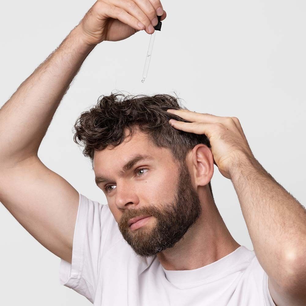 Un homme tient une pipette au-dessus de sa tête. Application du sérum.