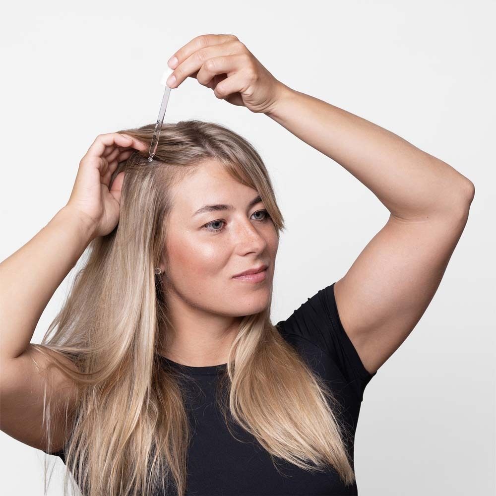 Femme avec pipette à la racine des cheveux. Cheveux blonds, haut noir.