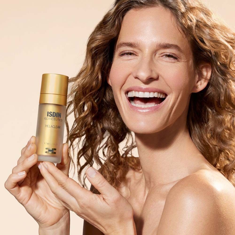 Femme tenant un flacon de sérum. Elle sourit. ISDINCEUTICS Melaclear Sérum.