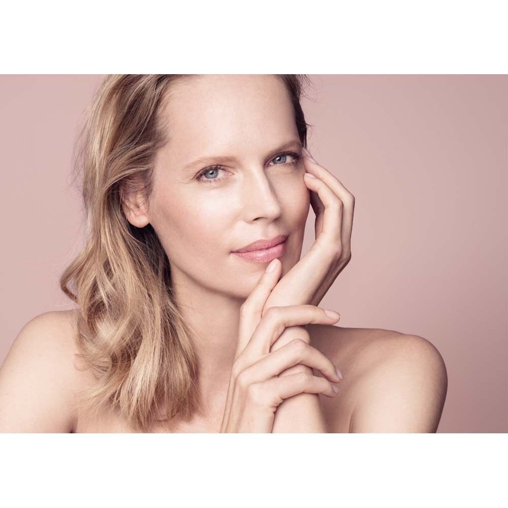 Portrait d'une femme aux cheveux blonds. Elle touche son visage avec ses mains. Fond rose.