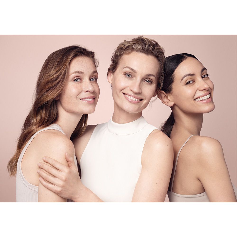 Trois femmes souriantes devant un fond rose. Elles portent des vêtements clairs.