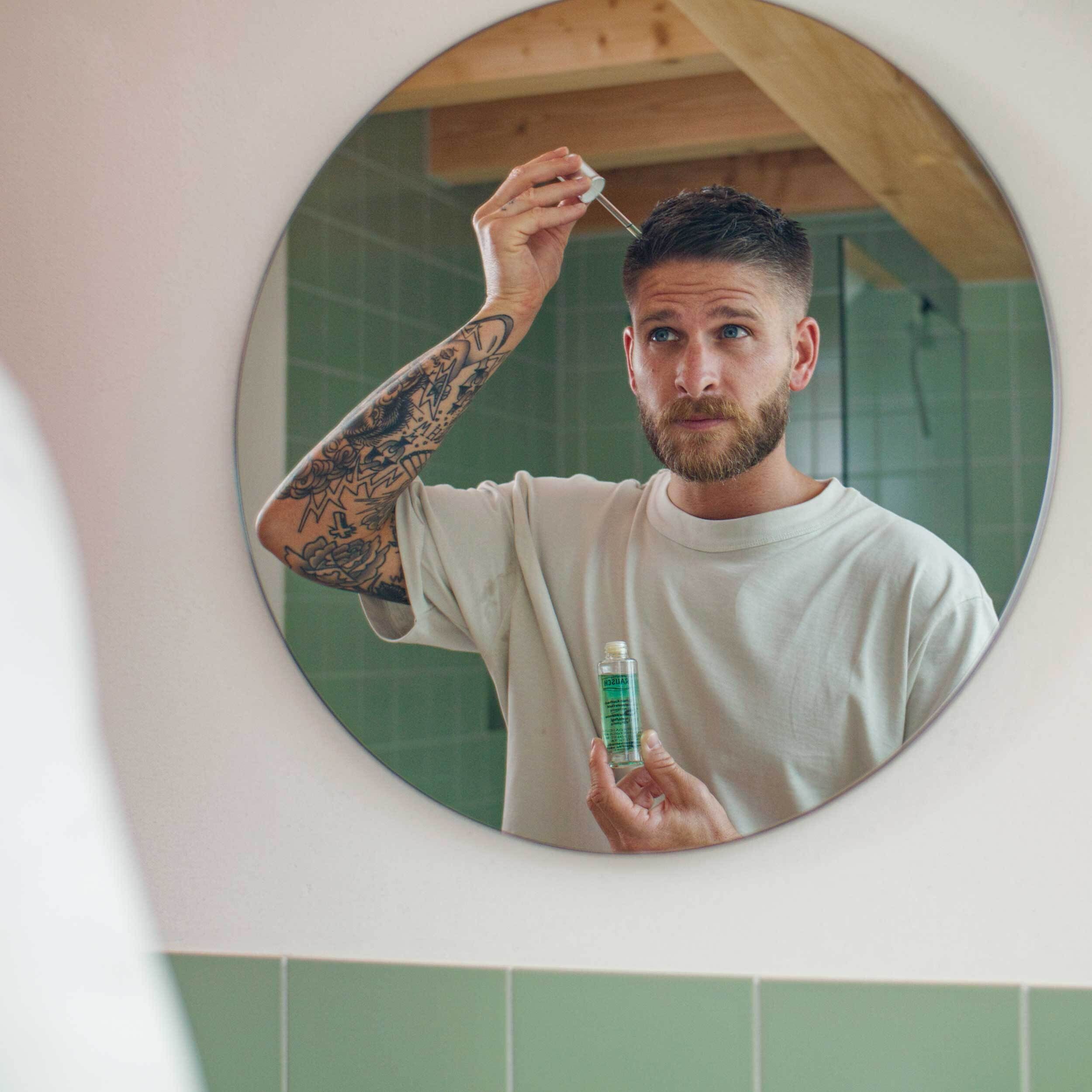 Homme tatoué applique le RAUSCH Coffein-Kopfhaut-Intensiv-Fluid avec pipette sur le cuir chevelu.