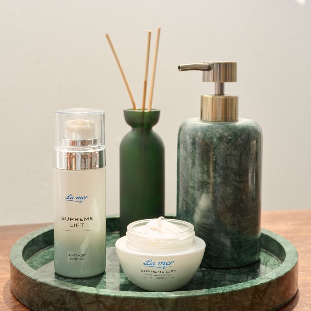 Sérum et crème La mer Supreme Lift Anti-Age sur plateau. Décoration verte. Flacons et pots.