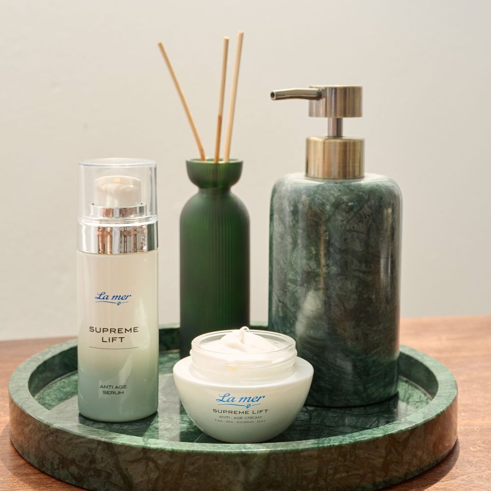 Arrangement de produits : sérum, crème La mer SUPREME LIFT et autres produits sur un plateau vert.