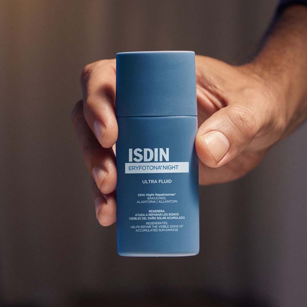 Personne tenant un flacon bleu ISDIN Eryfotona Night Ultra Fluid. Étiquette du produit clairement visible.