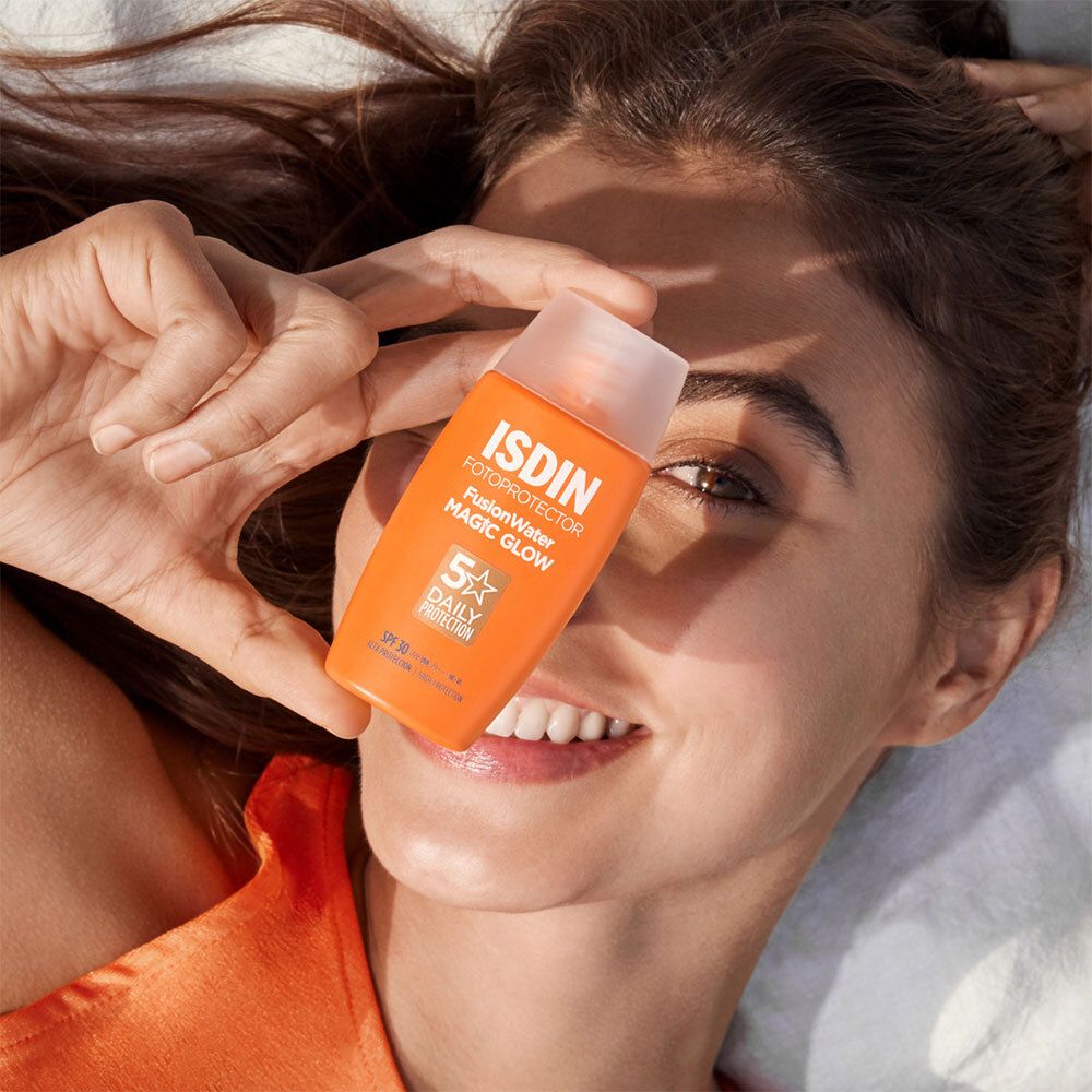 Femme tenant un flacon orange devant son visage. ISDIN Fotoprotector Fusion Water Magic Glow LSF 30.