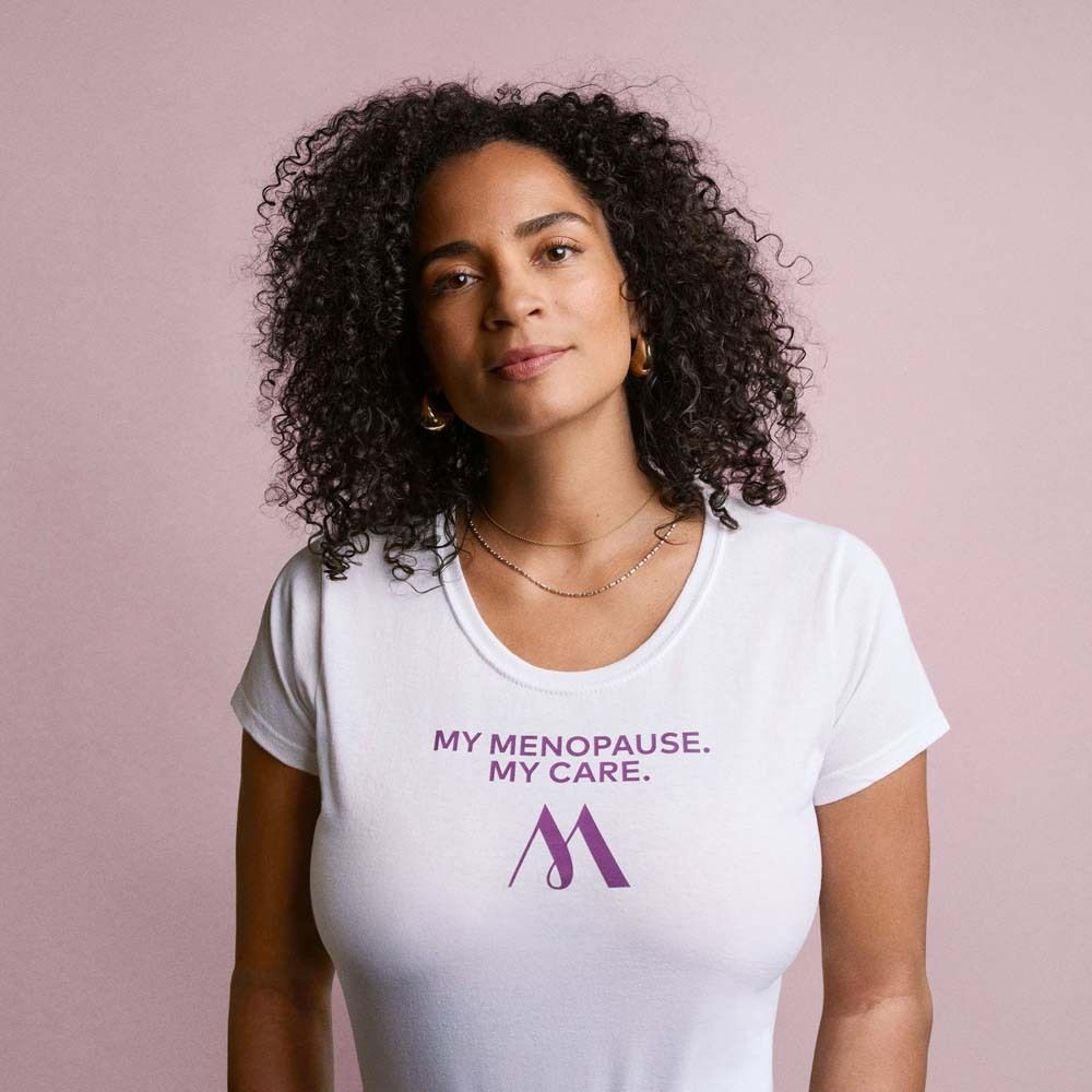 Femme en t-shirt blanc. Impression : My Menopause. My Care. Logo : M violet. Fond rose.