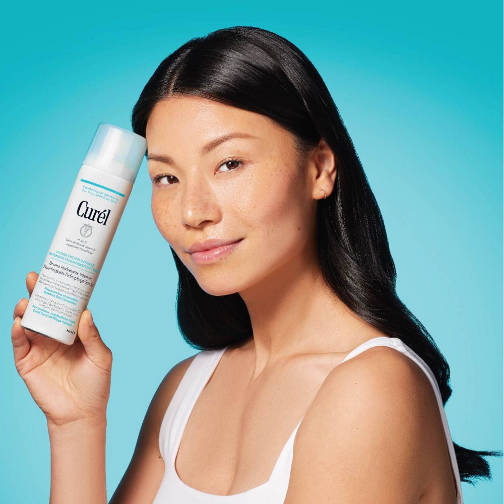 Femme asiatique tenant un spray blanc avec un bouchon bleu clair. Inscription : Curél. Pour peaux sèches et sensibles. Fond bleu.