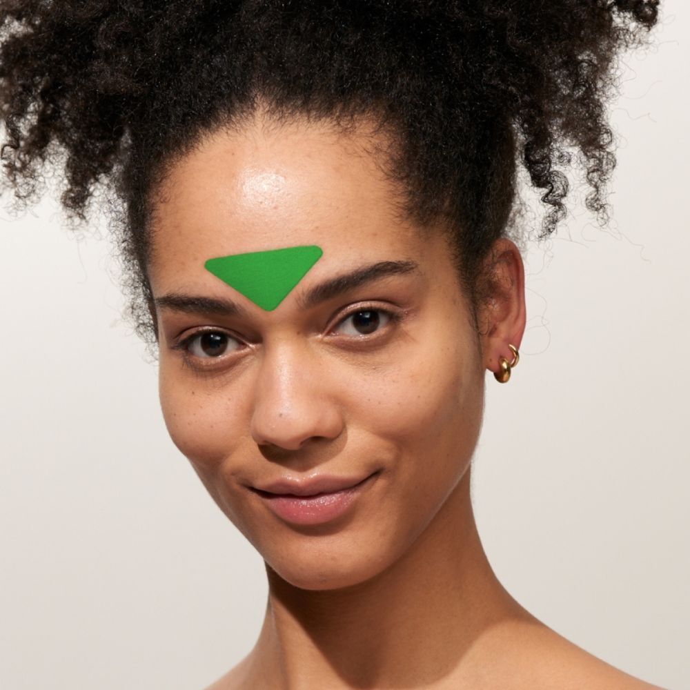 Femme portant un patch visage vert en forme de triangle à l'Aloe Vera sur le front.