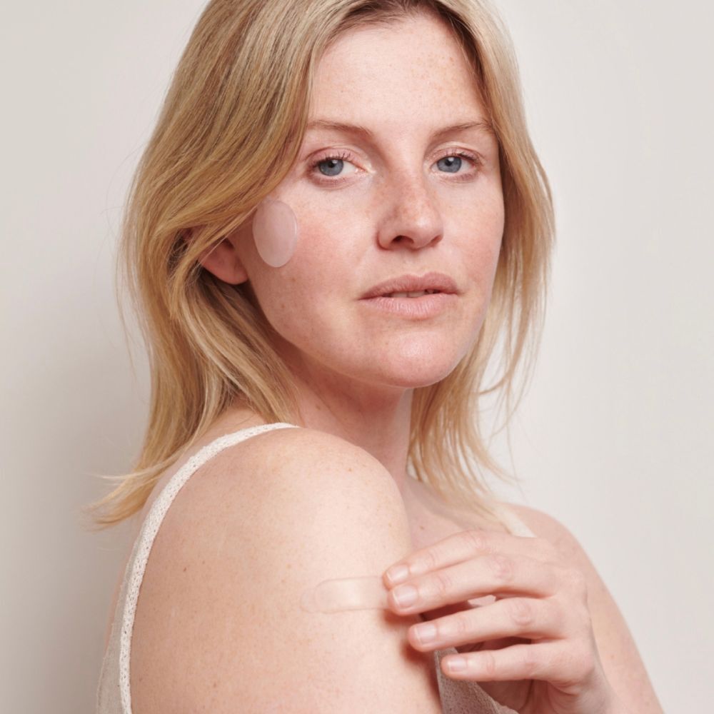 Femme avec un coussinet cicatriciel sur la joue et un coussinet oblong sur le bras. Peau claire, cheveux blonds.