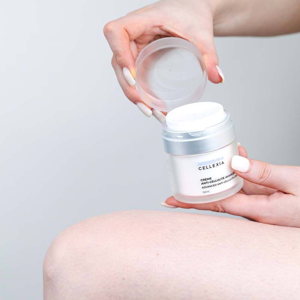 Mains tenant un pot et un couvercle de crème. Inscription: Cellexia, Crème Anti-Cellulite Avancée, Advanced Anti-Cellulite Cream, 50ml.
