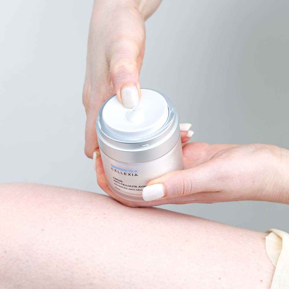 Mains tenant un pot de crème. Inscription: Cellexia, Crème Anti-Cellulite Avancée, Advanced Anti-Cellulite Cream, 50ml.
