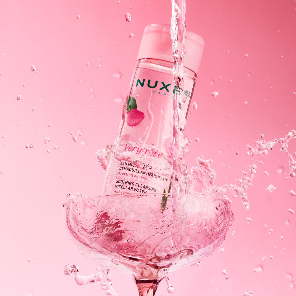 Nuxe Very Rose eau micellaire dans un verre. L'eau éclabousse. Fond rose.