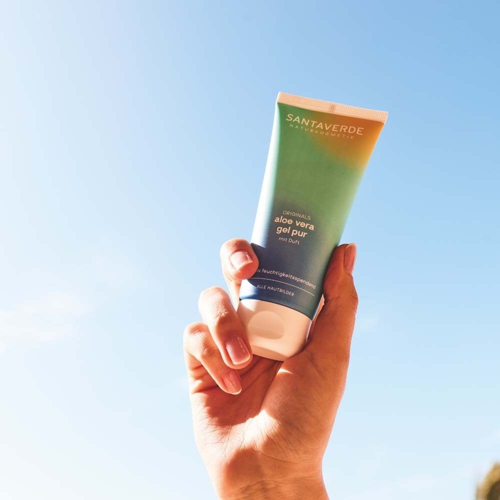 Main tenant un tube de gel aloe vera pur parfumé SANTAVERDE Naturkosmetik ORIGINALS. Ciel bleu en arrière-plan.