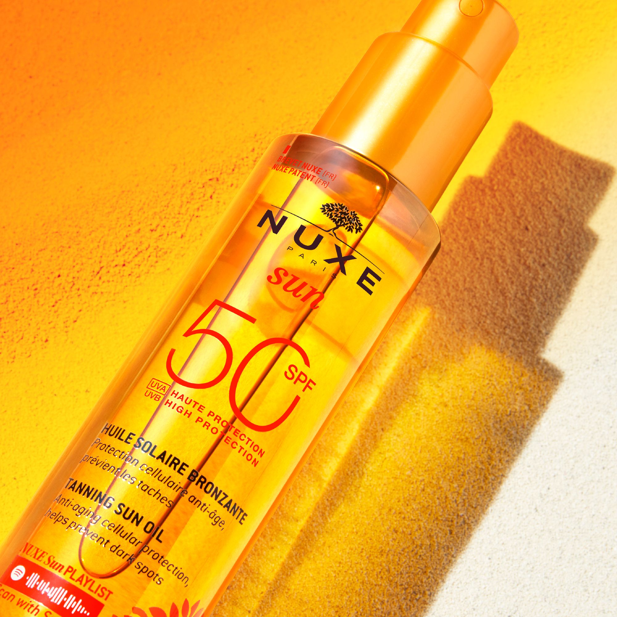 Flacon d'huile NUXE Sun SPF 50. Fond orange. Étiquette du produit avec texte.