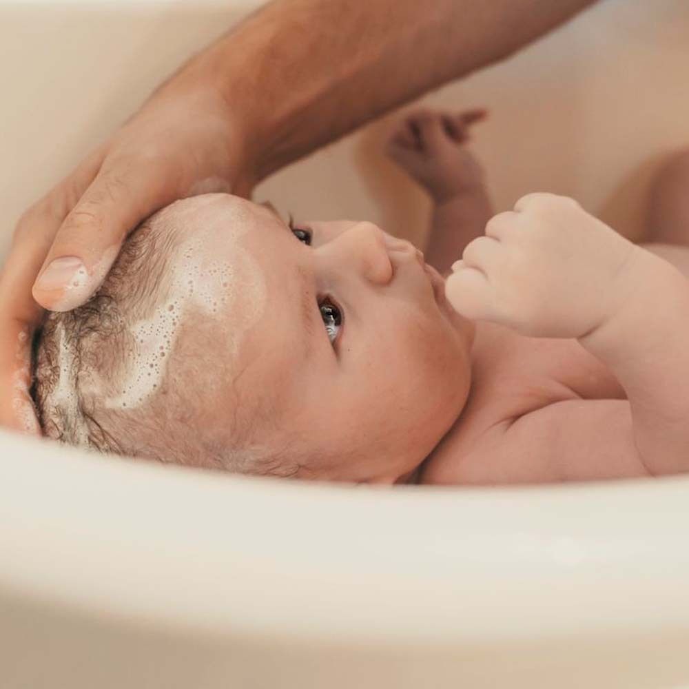 Bébé dans le bain. Une main lave les cheveux du bébé avec de la mousse.