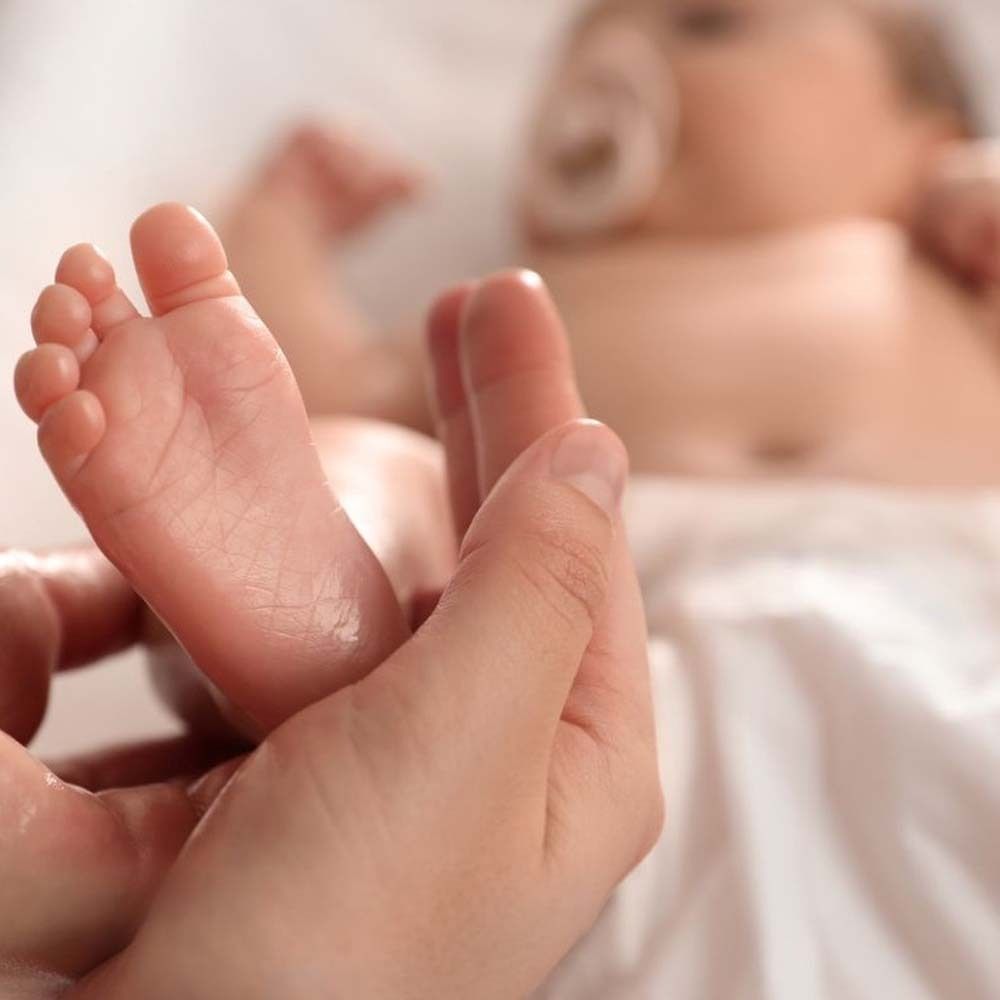 Gros plan sur un pied de bébé dans une main. Le pied est légèrement huilé.