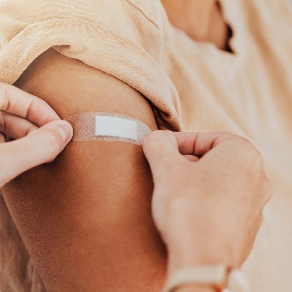 Personne applique un pansement transparent sur un bras. Le pansement est rectangulaire et transparent.