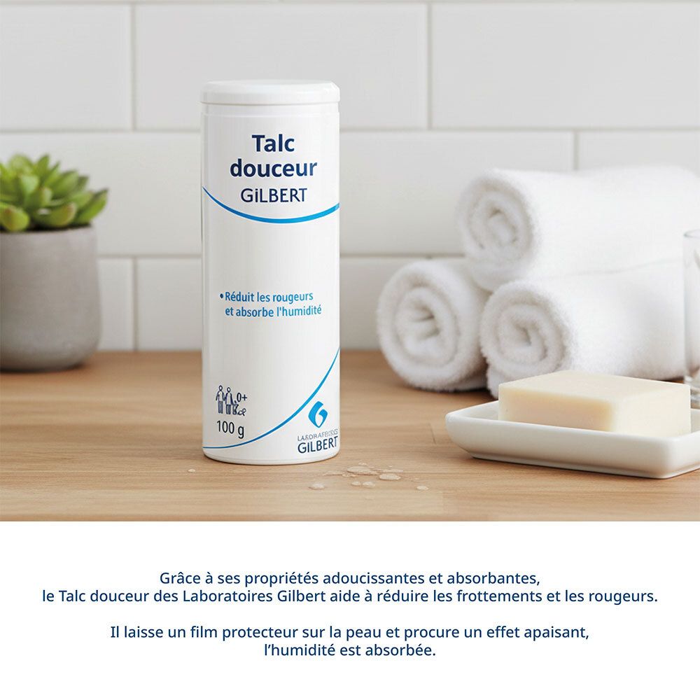 Flacon blanc de talc GILBERT. Inscription: Talc douceur. 100 g. Sur une table avec serviettes et savon.