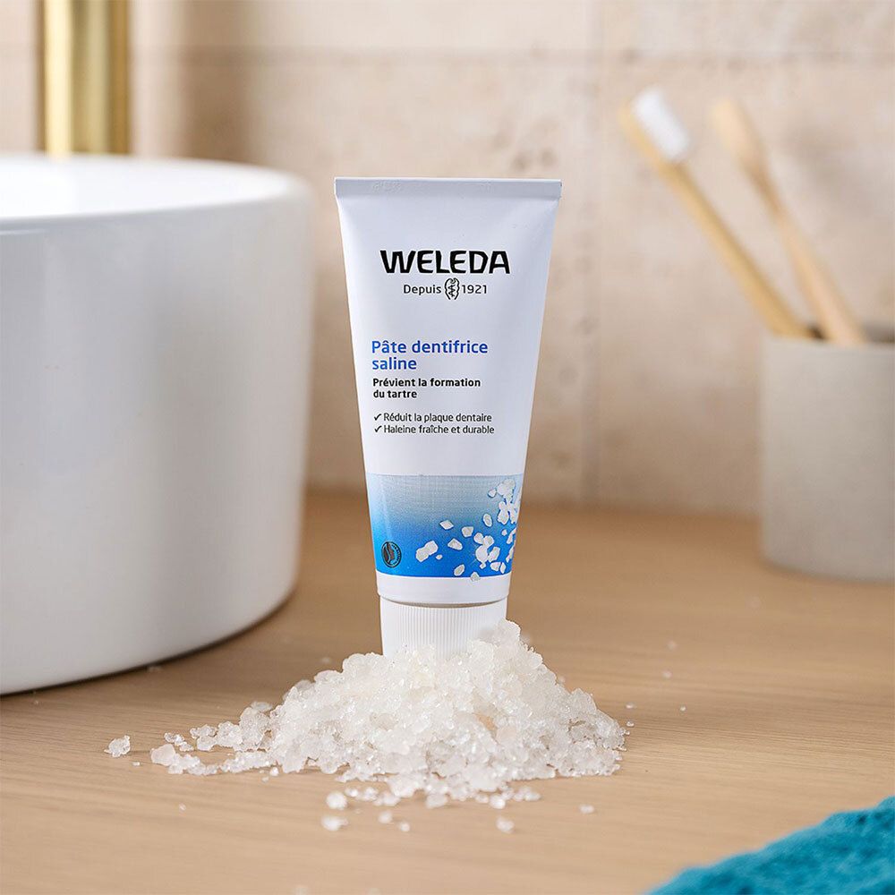Tube blanc avec texte bleu. WELEDA, Pâte dentifrice saline. Sur table avec sel. Fond de salle de bain.