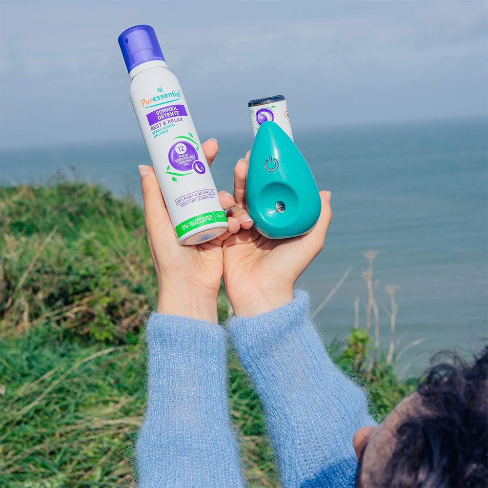 Mains tenant un diffuseur vert et un spray. En arrière-plan, la mer et le ciel.