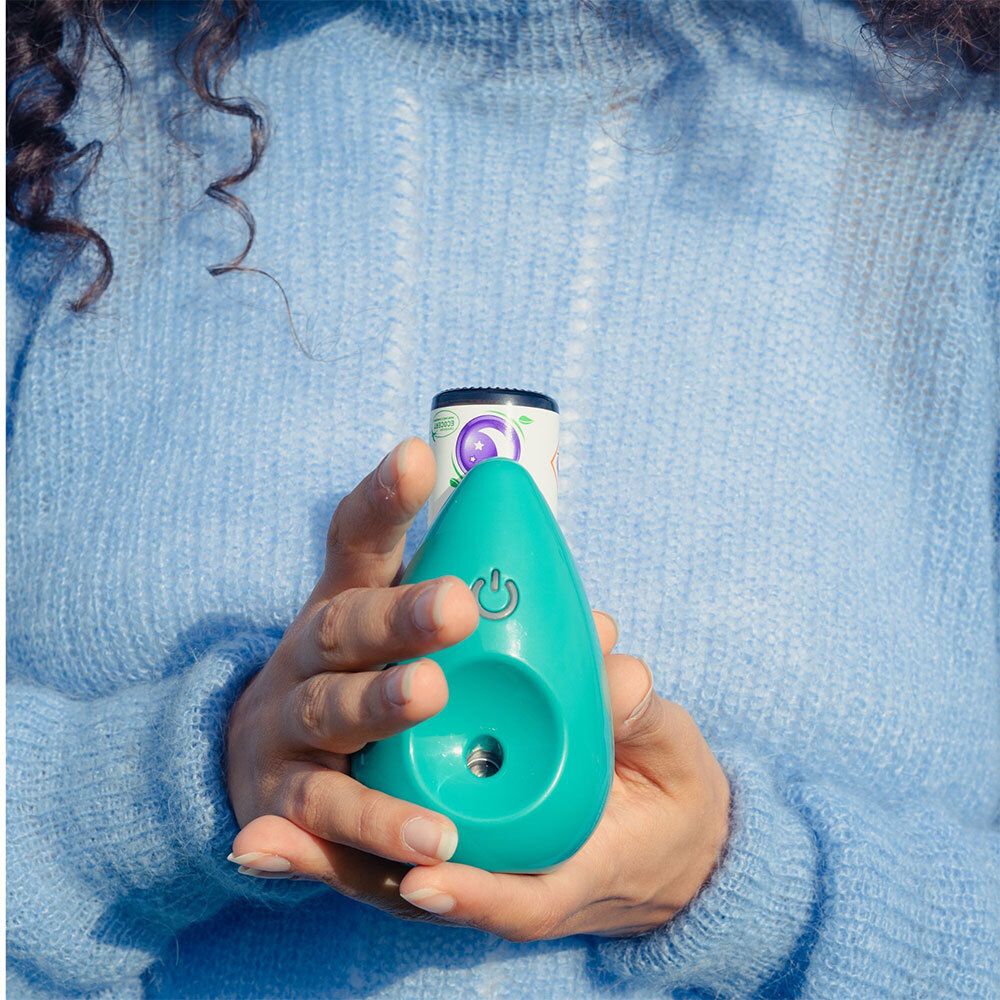 Mains tenant un diffuseur vert et un spray. En arrière-plan, la mer et le ciel.
