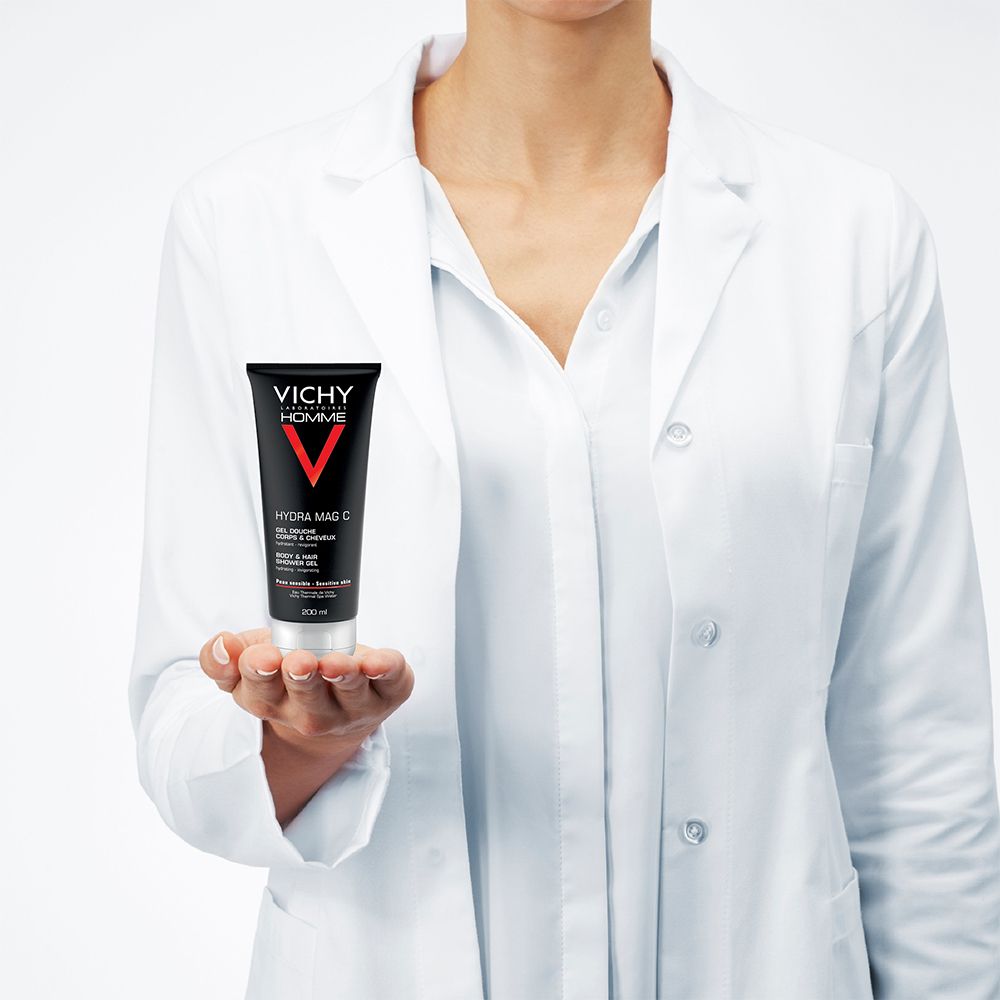Personne tenant un tube Hydra Mag C. Tube noir avec V rouge et bouchon blanc. Inscription: Vichy Homme, Hydra Mag C, Gel Douche.