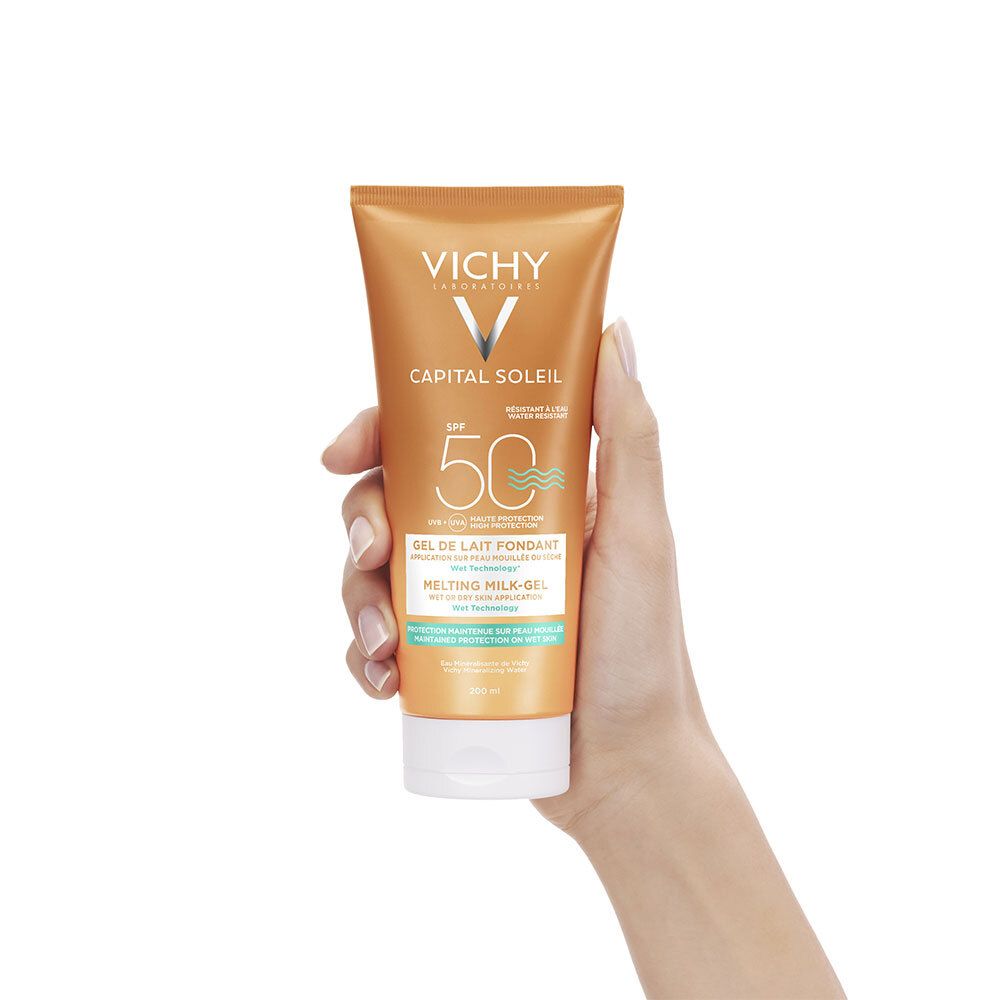 Main tenant un tube orange VICHY Capital Soleil avec SPF 50. Nom du produit et logo visibles.