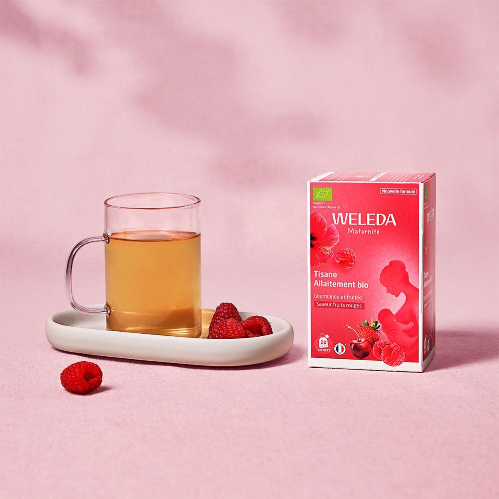 Verre de thé, fruits et boîte WELEDA Tisane Allaitement bio. Fond rose.
