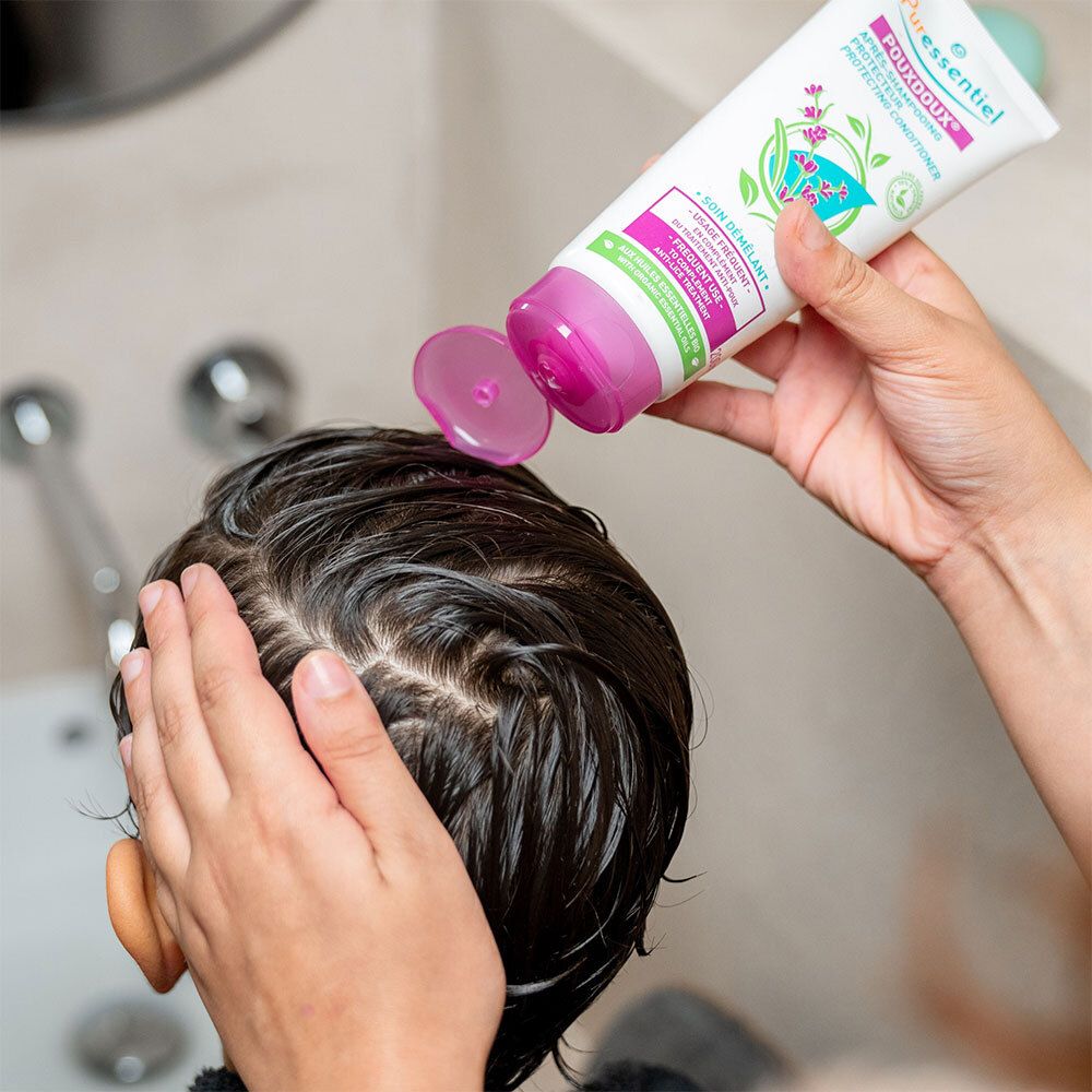 Personne verse le produit d'un tube sur la tête d'un enfant. Tube avec bouchon violet. Inscription: POUXDOUX®.