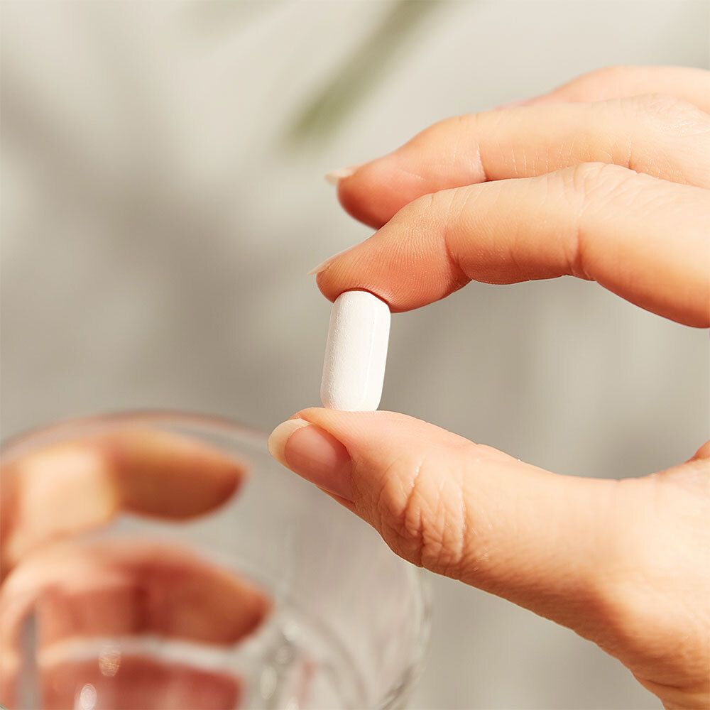 Main tenant un comprimé ovale blanc. Verre d'eau en arrière-plan.